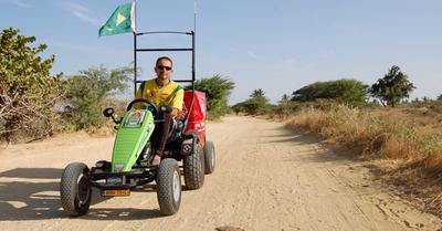 Pedal Joe riding a BERG offroad pedal kart with flag and cargo box on dusty dirt road
