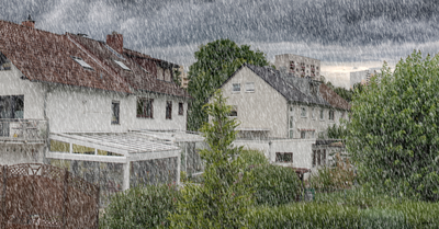 Banner af boligområde med huse og træer under en kraftig regnbyge og mørke skyer
