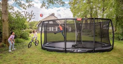 Children playing around a BERG Champion trampoline banner in a green garden