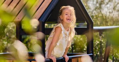Kind speelt op de BERG PlayTower in een groene tuin.
