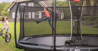 Banner with kids playing near a BERG Champion InGround trampoline with safety net in the garden