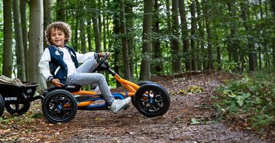 Kind rijdt op een BERG Buddy B-Orange skelter met aanhanger in een bos