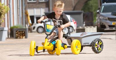 Enfant conduit un kart à pédales BERG Buzzy jaune avec remorque dans un quartier résidentiel