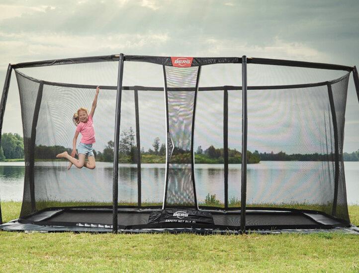 Niño salta en una cama elástica BERG Ultim Elite de uso público junto a un lago