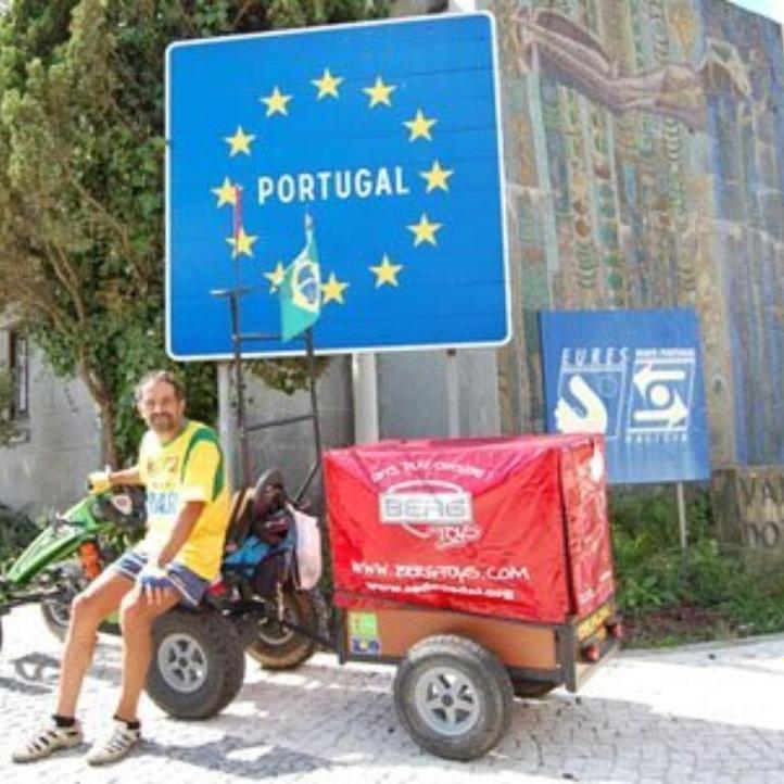 Pedal Joe con su coche de pedales BERG y remolque junto al cartel fronterizo de Portugal