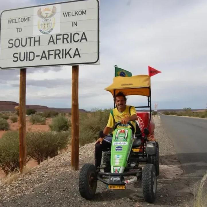 Pedal Joe con su coche de pedales BERG junto al cartel de bienvenida de Sudáfrica en una carretera desierta
