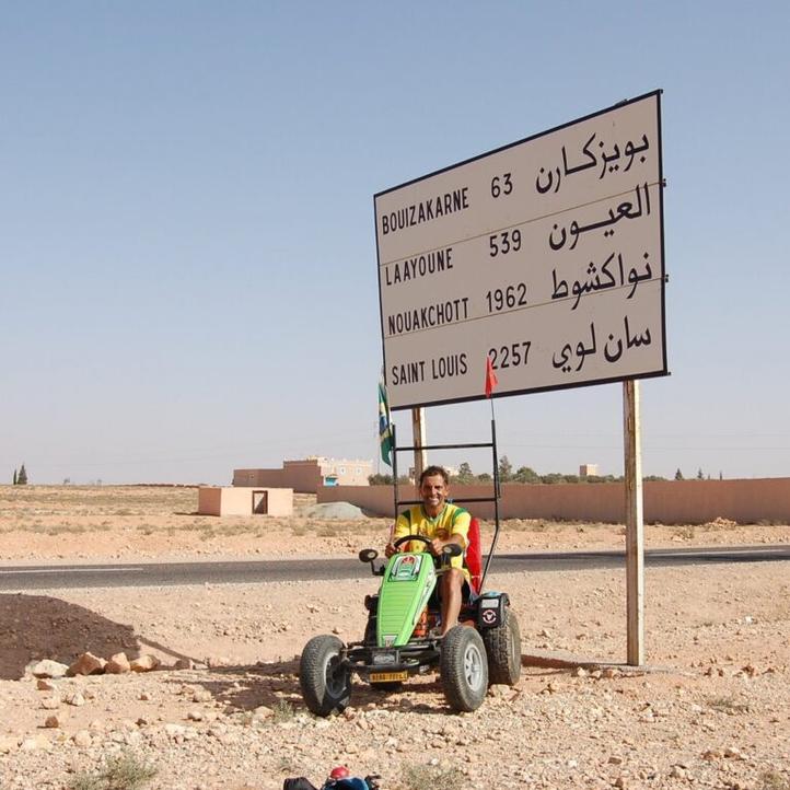 Pedal Joe con su coche de pedales BERG junto a un cartel de distancias en el desierto del oeste de África hacia Mauritania
