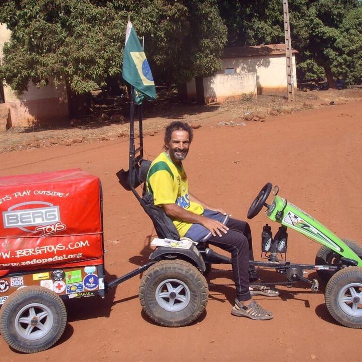 Pedal Joe con su coche de pedales BERG y remolque en un camino de tierra roja en Bamako, Malí