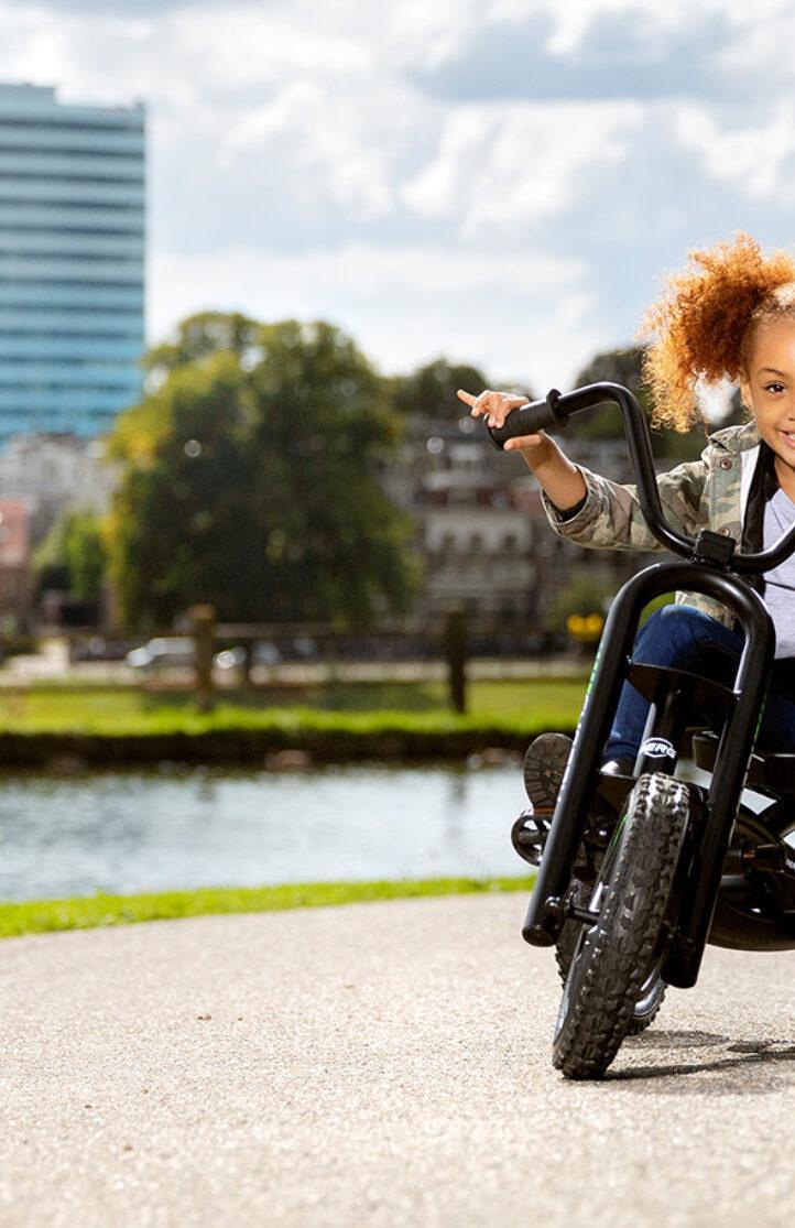 Kind rijdt op een BERG driewieler over een fietspad langs het water in de stad
