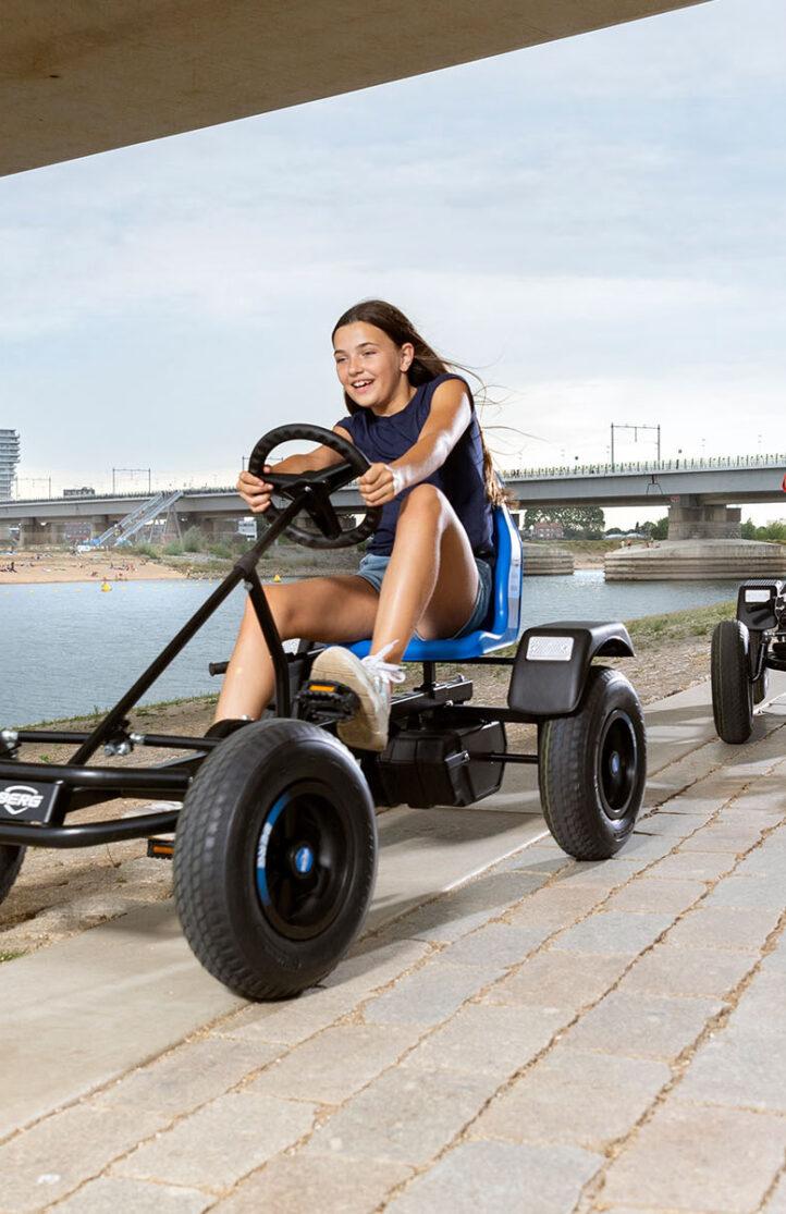 Twee kinderen racen op BERG skelters langs het water onder een brug