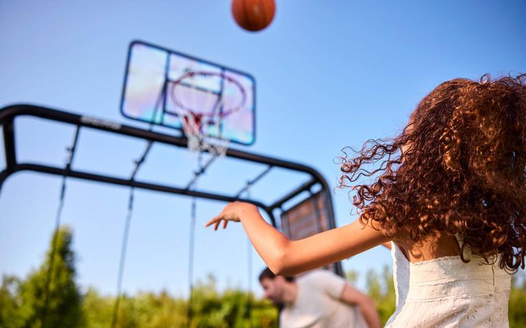 Jente kaster ball i kurven på BERG PlayBase lekestativ på en solrik dag