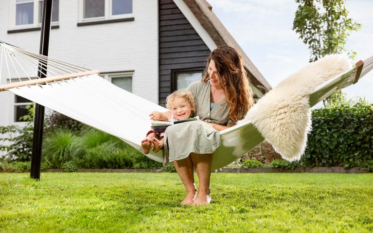 Mor leser for barnet sitt i en hengekøye festet til et BERG PlayBase lekestativ i hagen