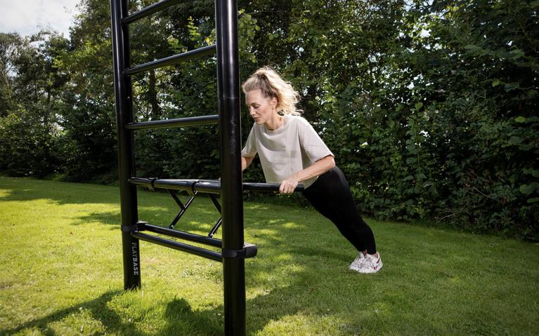 Frau macht Liegestütze an der BERG PlayBase im Garten als Teil des Outdoor-Krafttrainings