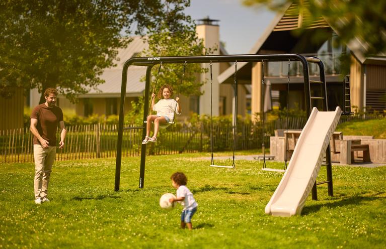 Banner met kinderen spelend op BERG PlayBase met schommel en glijbaan in zonnige tuin