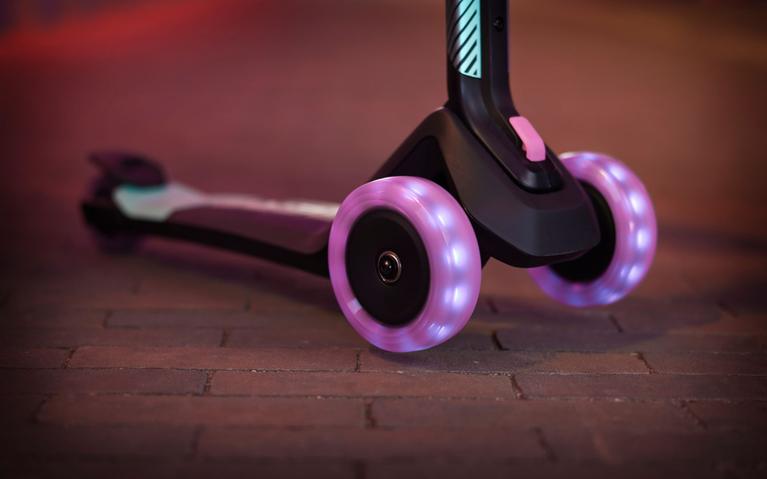 Närbild på en BERG Nexo Foldable sparkcykel med lysande lila hjul på gatsten