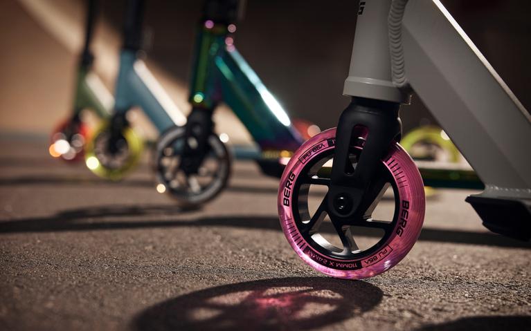 Närbild på framhjulet av BERG Proxus stunt-sparkcykel med rosa fälg på asfalt