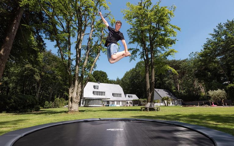 Jugendlicher springt hoch auf einem eingelassenen BERG Trampolin im Garten einer modernen Villa