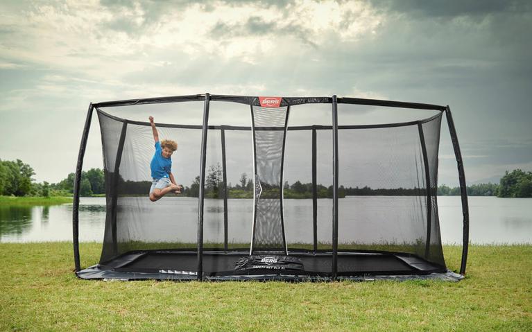 Kind springt op een BERG Ultim trampoline met veiligheidsnet aan het water onder een bewolkte lucht
