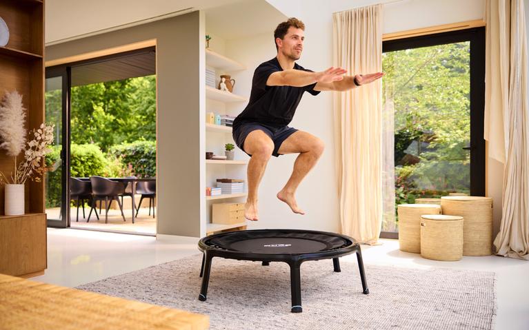 Man traint sprongkracht op een zwarte BERG fitness-trampoline in de woonkamer – effectief voor cardio en explosiviteit.