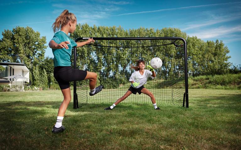 Dwie dziewczynki grają w piłkę nożną z bramką BERG SportsGoal banner na trawie