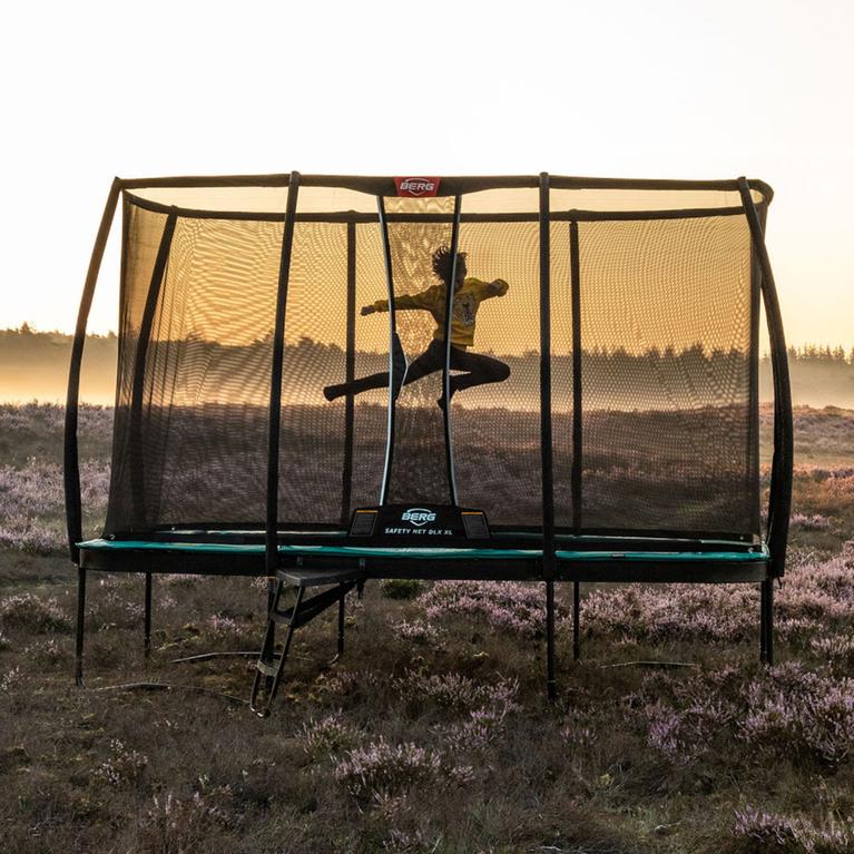 Enfant sautant sur un trampoline BERG Ultim Champion Regular avec filet Deluxe dans la nature au lever du soleil