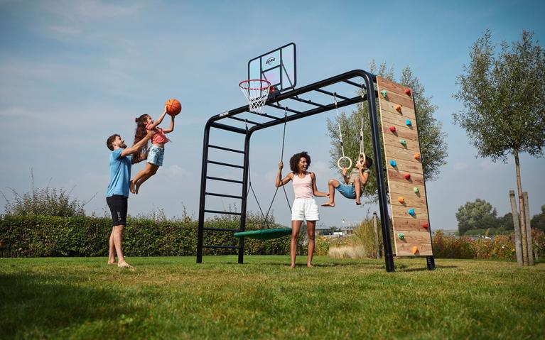 Gezin speelt op een BERG PlayBase met basketbal, schommel en klimwand in de tuin