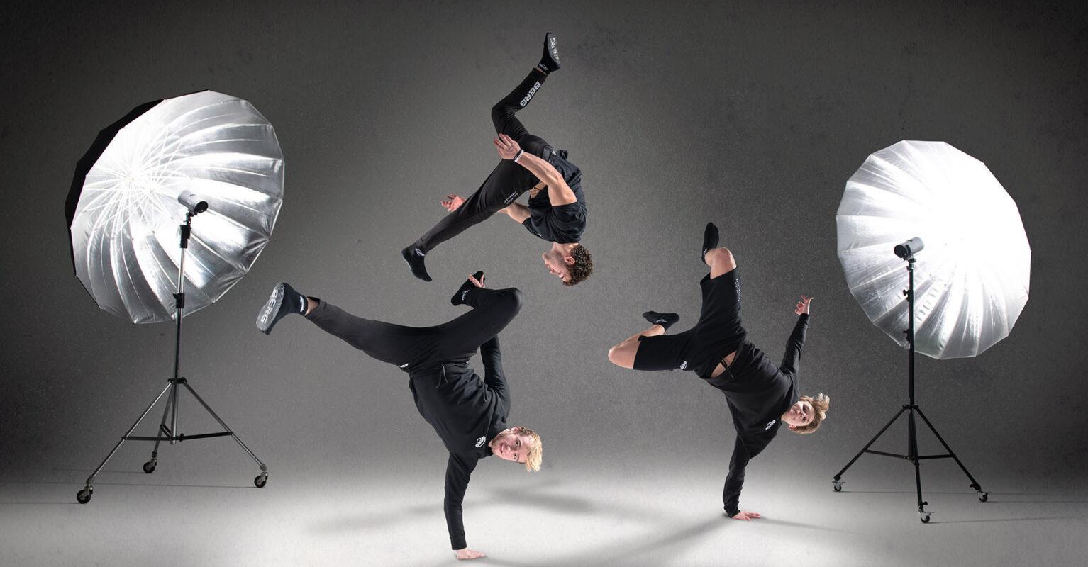 Kolme breakdance-tanssijaa esittää näyttäviä liikkeitä studiossa, jossa on suuret softbox-valot.