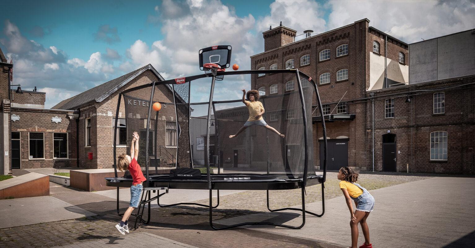 Kinderen spelen basketbal op een BERG trampoline met TwinHoop in een stedelijke omgeving