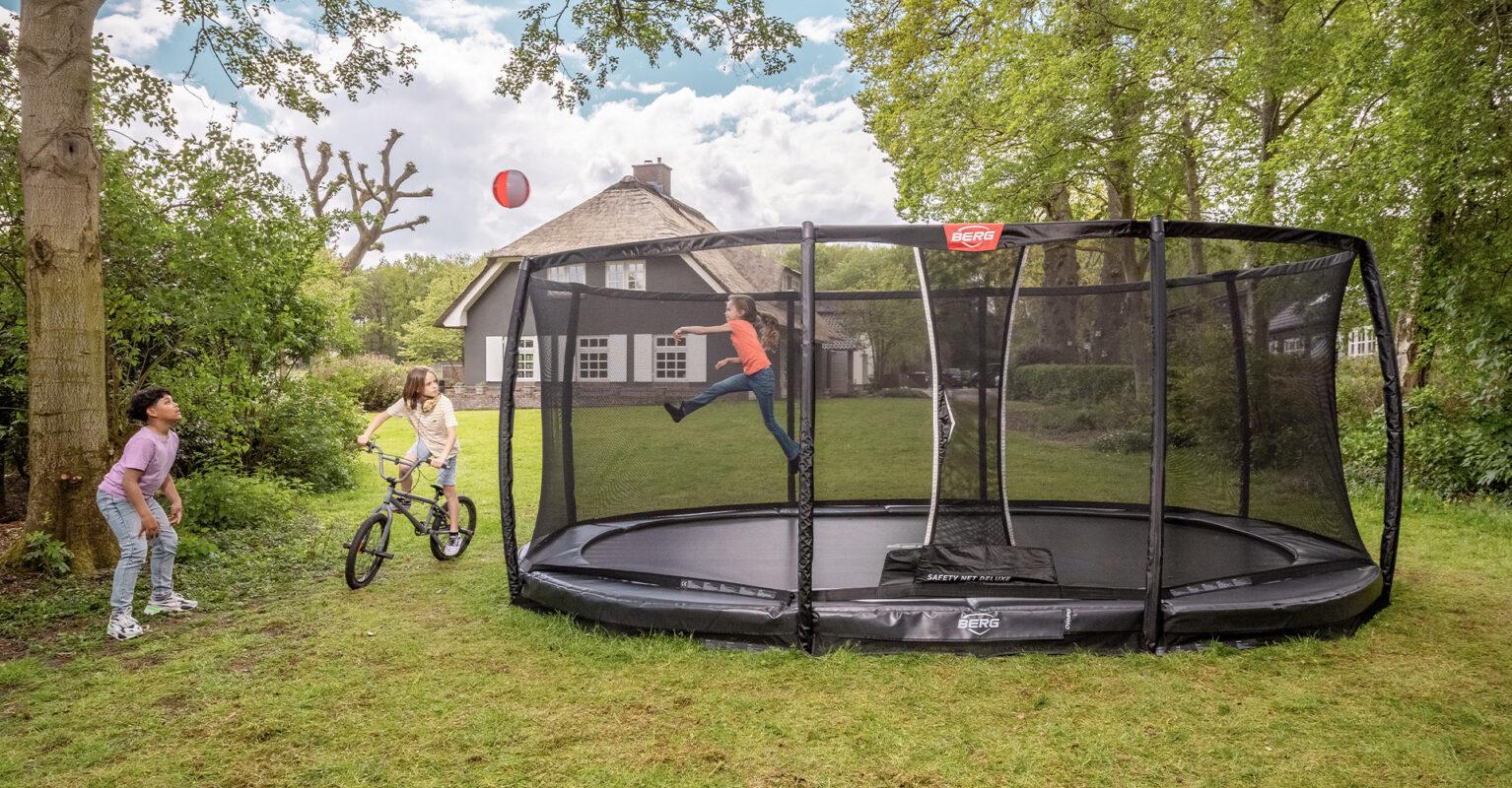 Children playing around a BERG Champion trampoline banner in a green garden