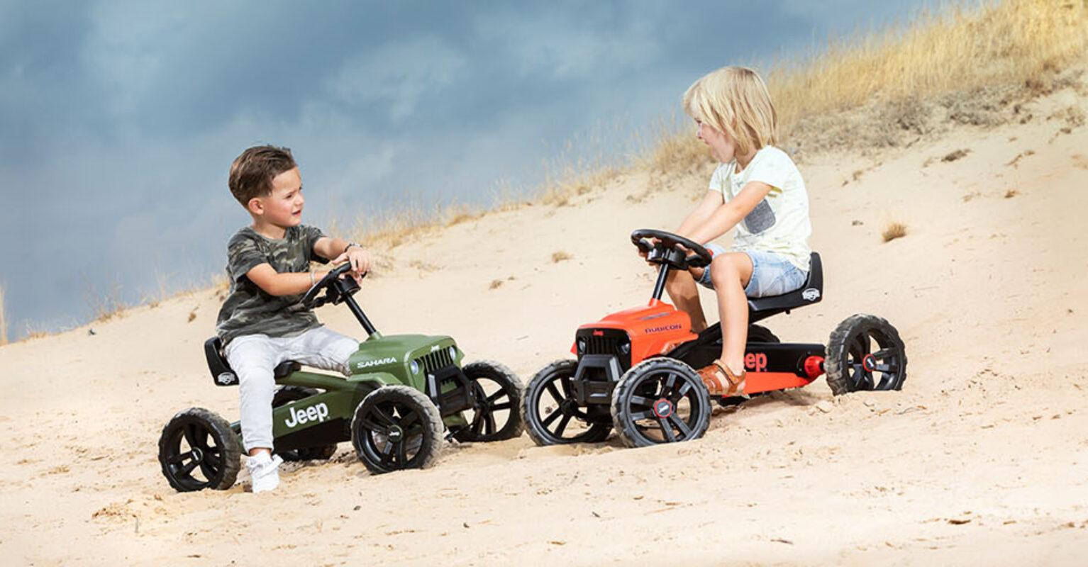 Twee kinderen racen op BERG Buzzy Jeep gocarts door het zand
