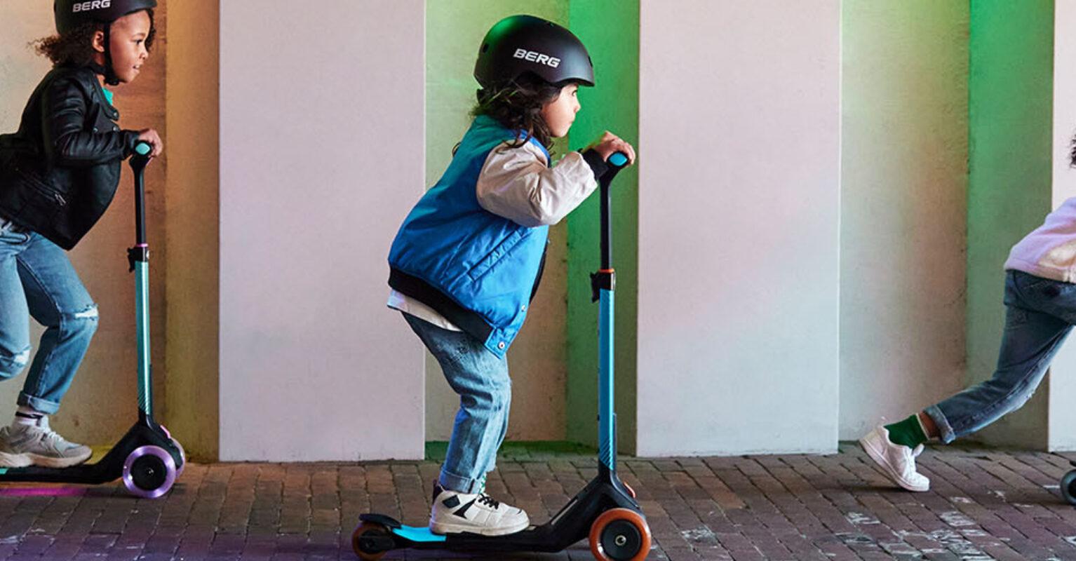Banner met drie kinderen op BERG Nexo stepjes rijdend onder kleurrijke verlichting