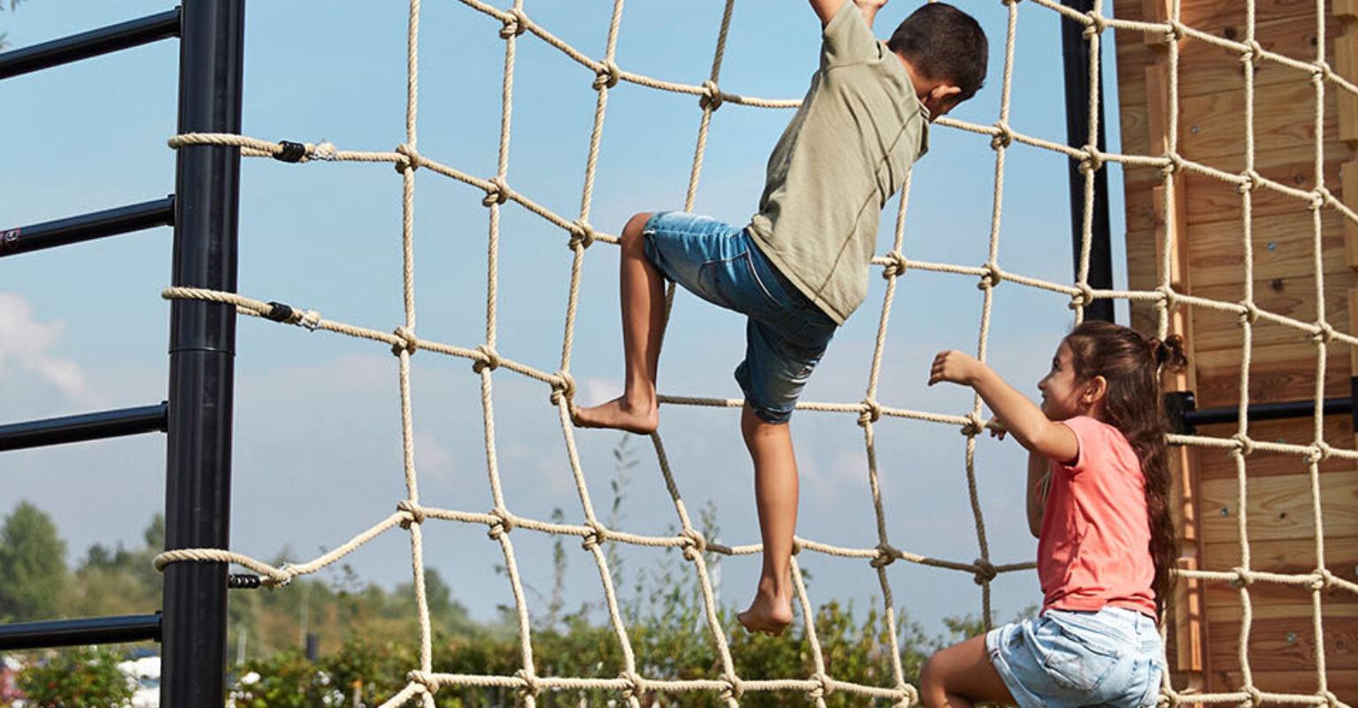 Banner med to barn som klatrer på et BERG PlayBase lekestativ med nett i hagen