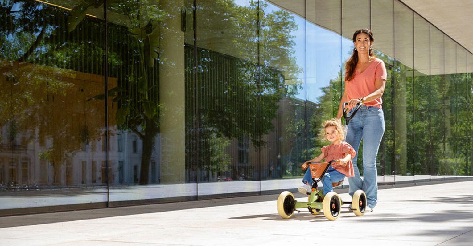 Ouder duwt kind op BERG Buzzy 2-in-1 skelter in een moderne omgeving